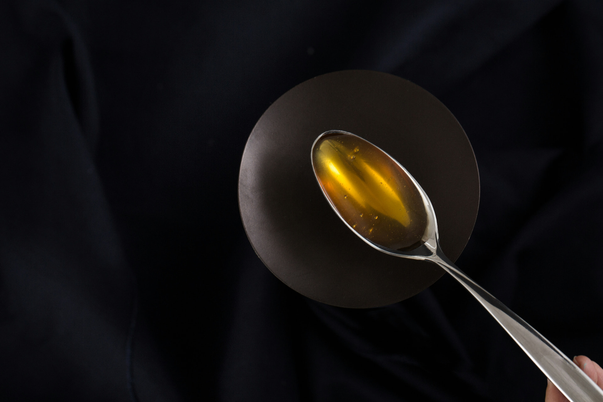 A spoon holding a glossy golden spherification pearl