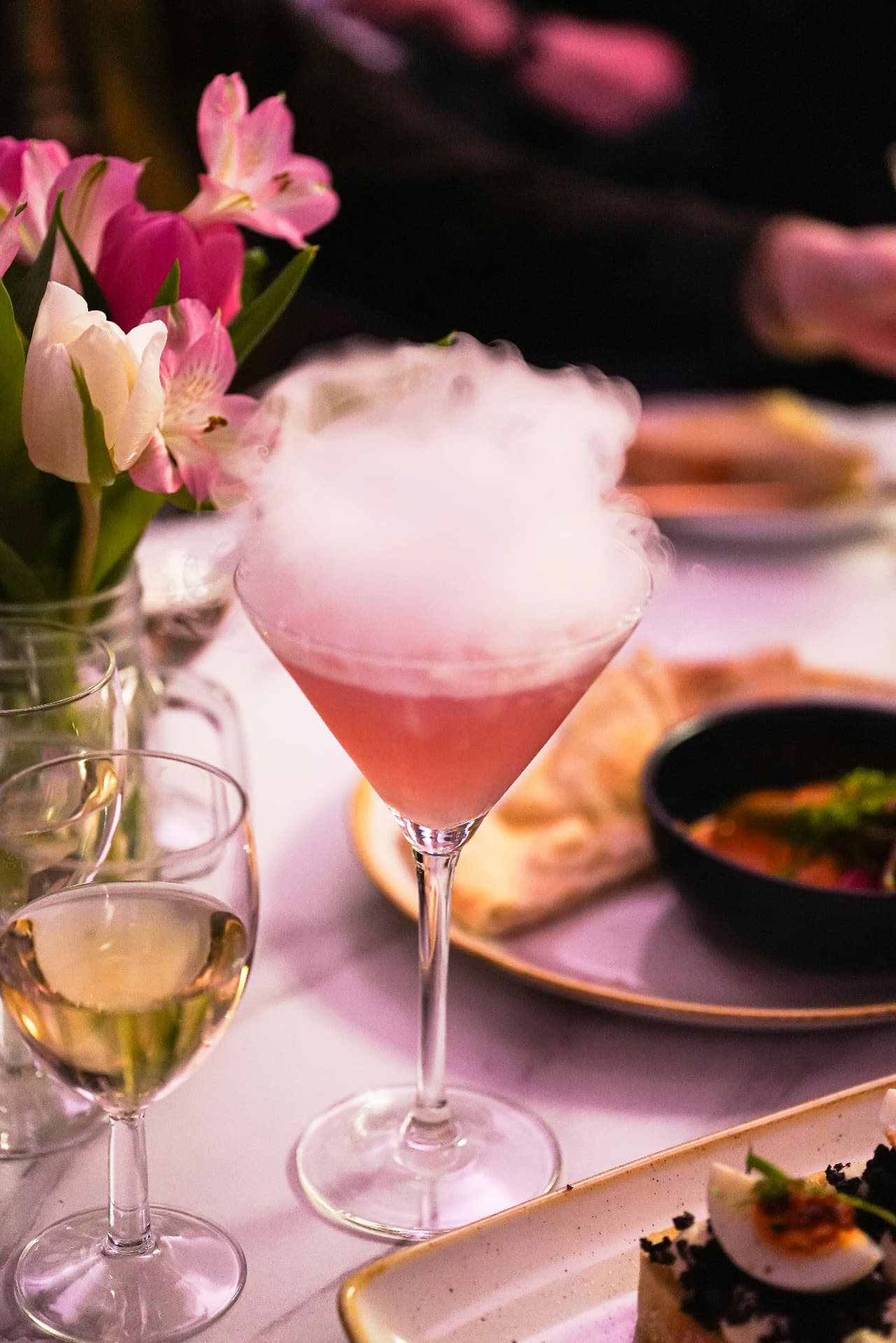 A pink cocktail releasing aromatic mist from dry ice